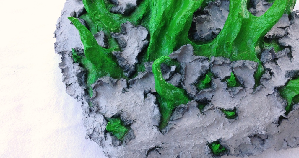 Detail of an original sculpture by MJ Seal made from paper mache that resembles spiky, spring green tentacles breaking out of a gray, papery skin