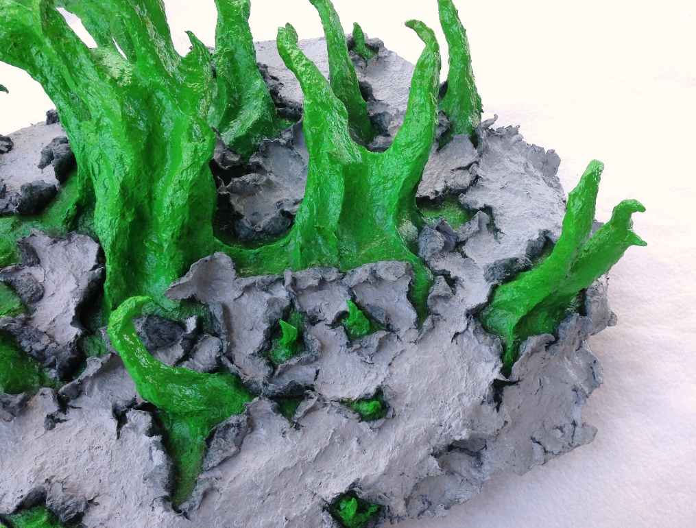 Detail of an original sculpture by MJ Seal made from paper mache that resembles spiky, spring green tentacles breaking out of a gray, papery skin