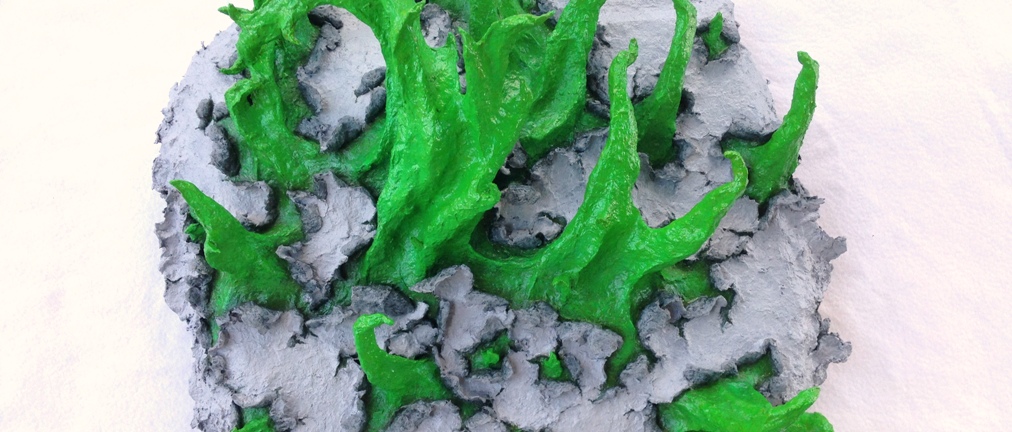 Detail of an original sculpture by MJ Seal made from paper mache that resembles spiky, spring green tentacles breaking out of a gray, papery skin