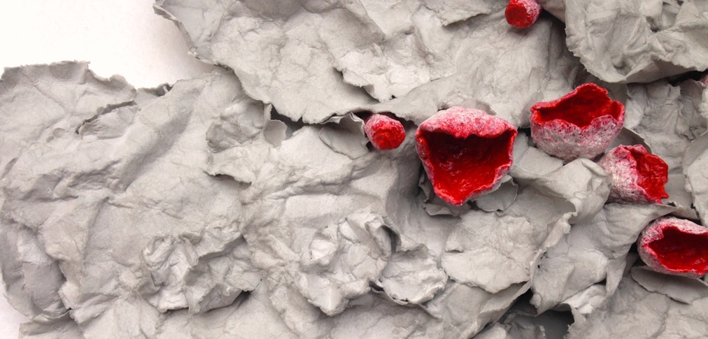 A paper mache sculpture by MJ Seal that resembles a cluster of Scarlet Cup Fungus emerging from a pile of dried, gray leaves