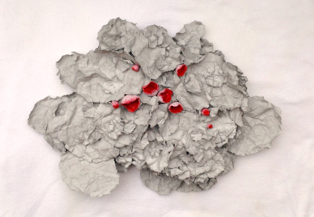 A paper mache sculpture by MJ Seal that resembles a cluster of Scarlet Cup Fungus emerging from a pile of dried, gray leaves