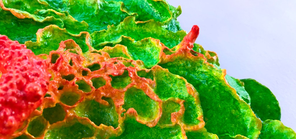 Detail of an abstract paper mache sculpture by MJ Seal that resembles a psychedelic lichen or flower with hues of viridian, chartreuse and coral red