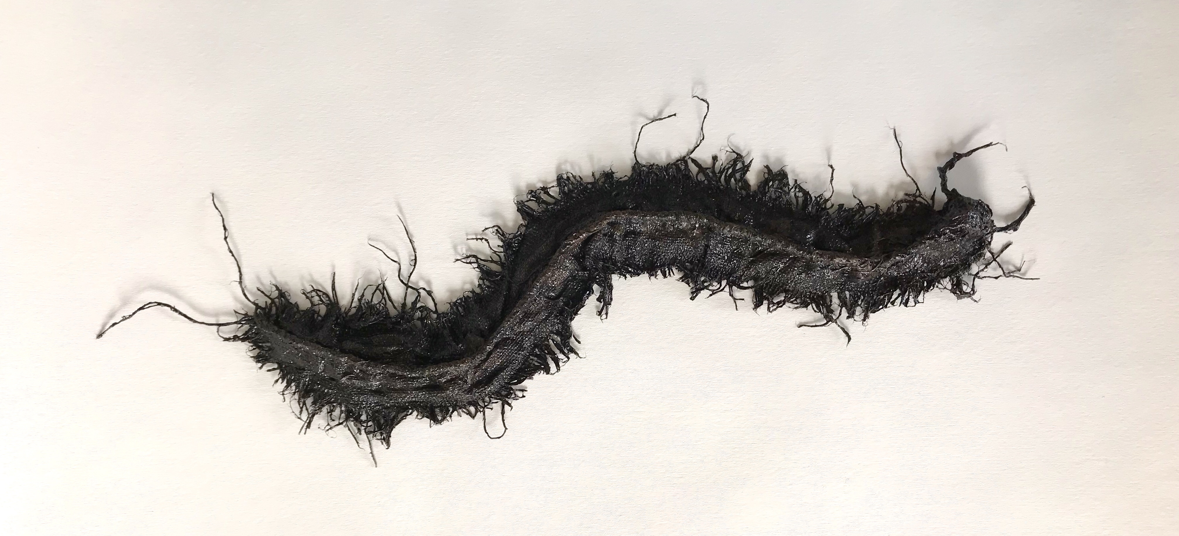 Full view of an abstract sculpture made from sackcloth by MJ Seal that resembles a giant, glistening, blackish brown centipede