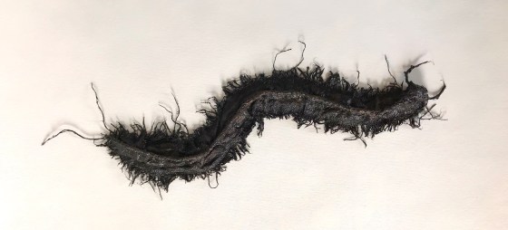 Full view of an abstract sculpture made from sackcloth by MJ Seal that resembles a giant, glistening, blackish brown centipede