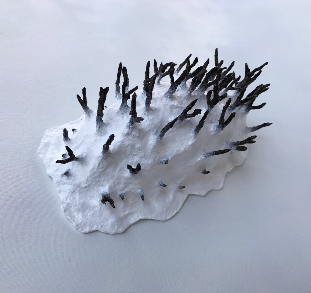 Anterior view of an abstract paper mache sculpture by MJ Seal that resembles a primitive white sea creature with black spikes poking out