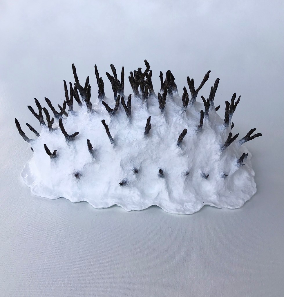 Side view of an abstract paper mache sculpture by MJ Seal that resembles a primitive white sea creature with black spikes poking out