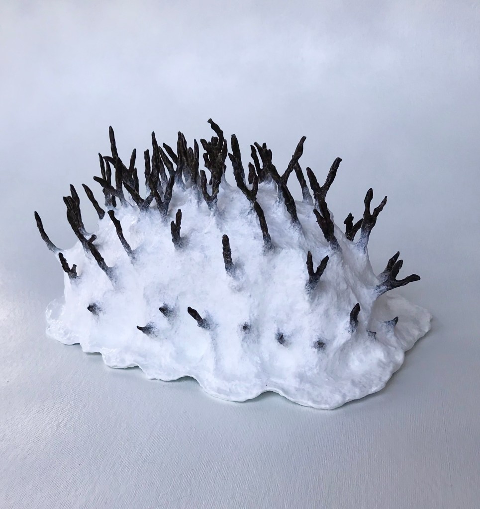 Side view of an abstract paper mache sculpture by MJ Seal that resembles a primitive white sea creature with black spikes poking out