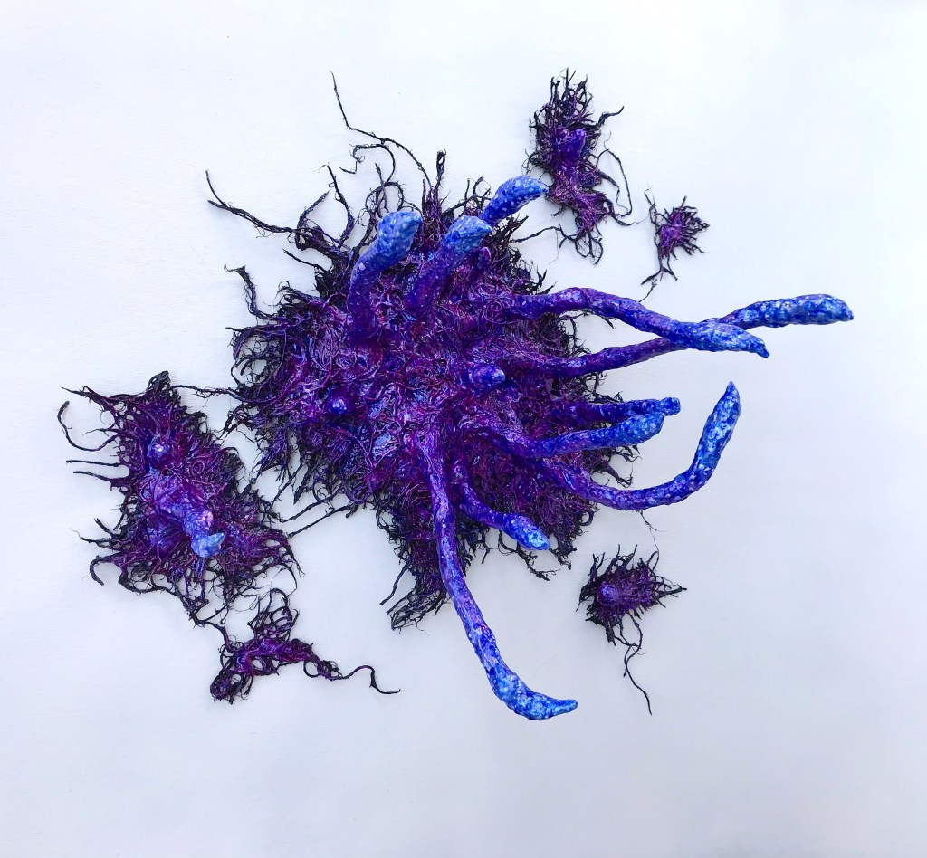Full view of an abstract paper mache sculpture by MJ Seal that resembles an iridescent octopus reaching through a wall