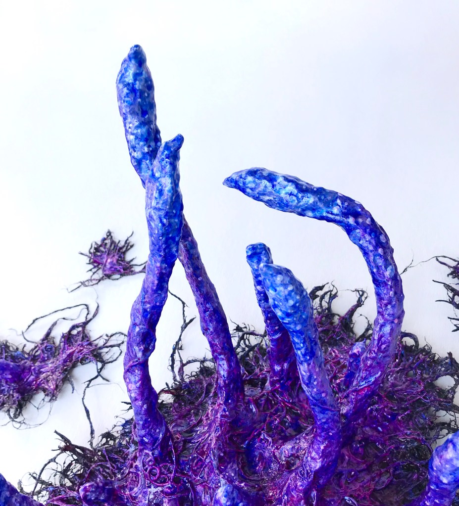 Detail of an abstract paper mache sculpture by MJ Seal that resembles an iridescent octopus reaching through a wall