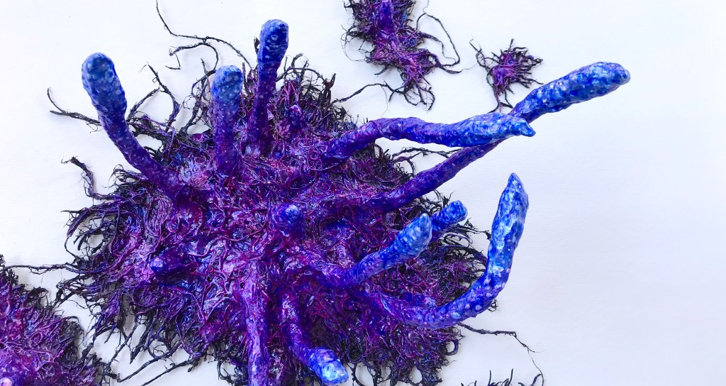 Detail of an abstract paper mache sculpture by MJ Seal that resembles an iridescent octopus reaching through a wall