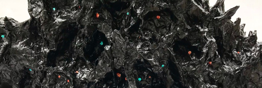 Close up detail of an abstract paper mache sculpture by MJ Seal that resembles a black thory mass of monstrous faces with glinting orange and blue eyes